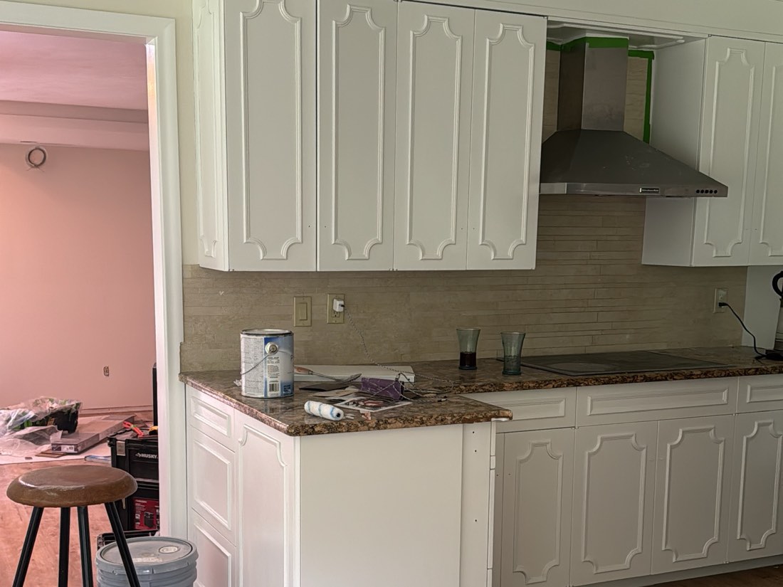Kitchen cabinets and peninsula sprayed white under a stainless hood