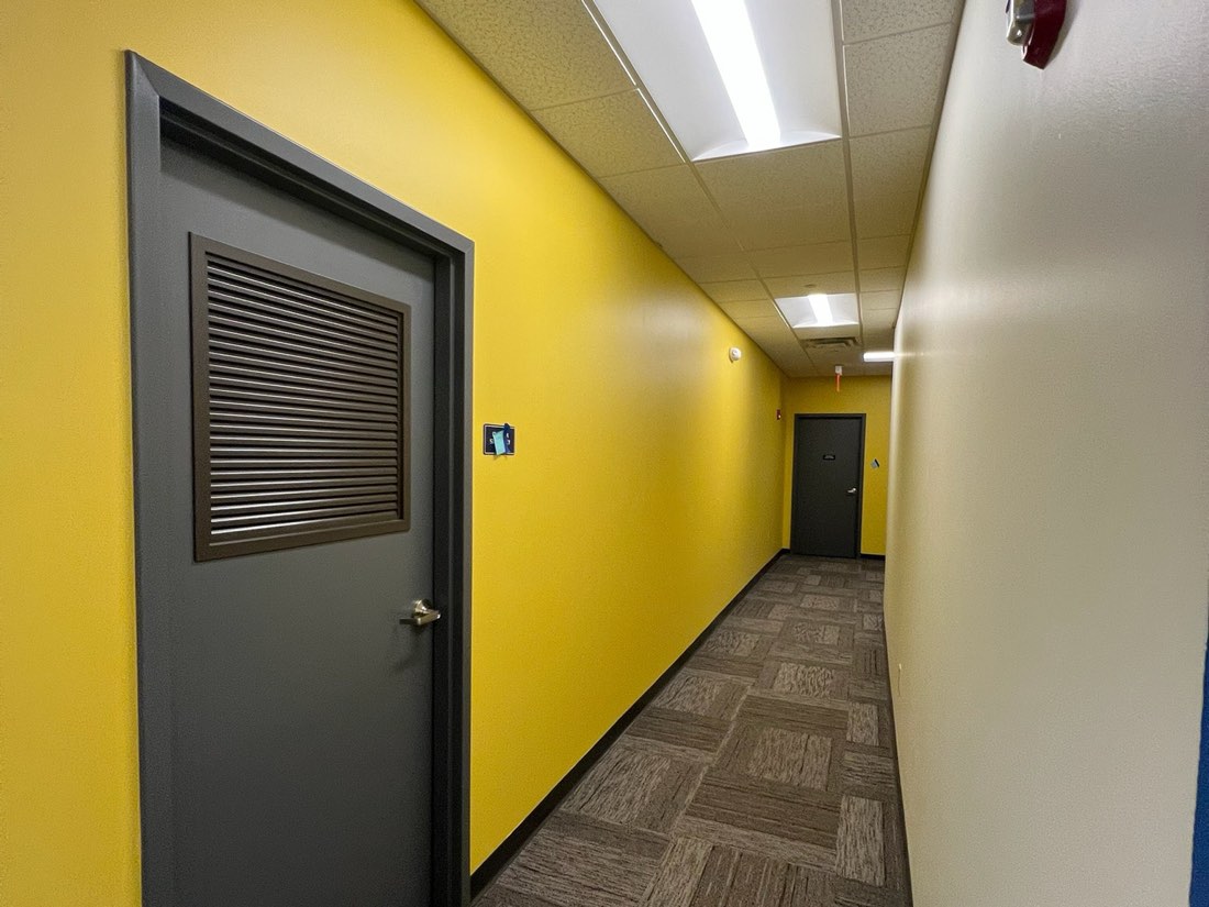 Commercial hallway with yellow walls and grey doors