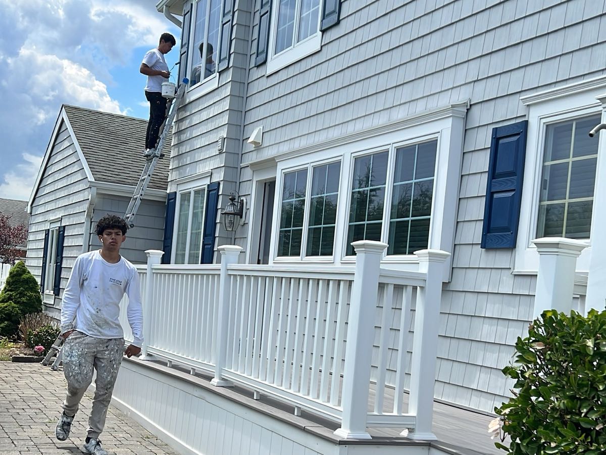 Prime Paint crew painting the exterior of a shingled home with white porch railings and navy shutters