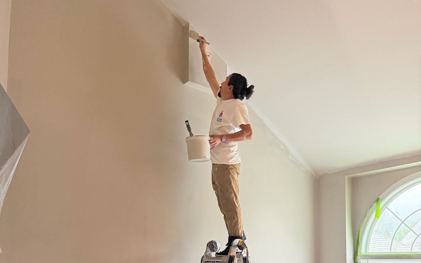 Prime Paint painter on a ladder cutting in a ceiling line with the room covered below